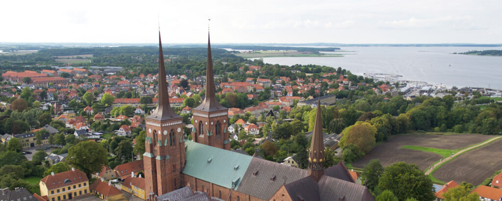 Flygfoto över Roskilde med den berömda Roskilde domkyrka i förgrunden och staden samt Roskilde fjord i bakgrunden.